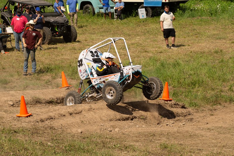 Baja car lifting a wheel between cones while judges and spectators watch