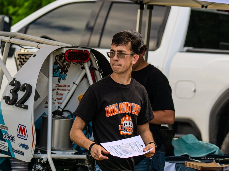 Team member holding a checklist beside the number 32 panel of the Baja car