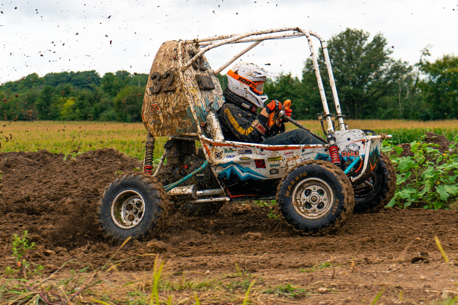 Side view of Baja car number 32 on a dirt track with its suspension loaded, green fields behind
