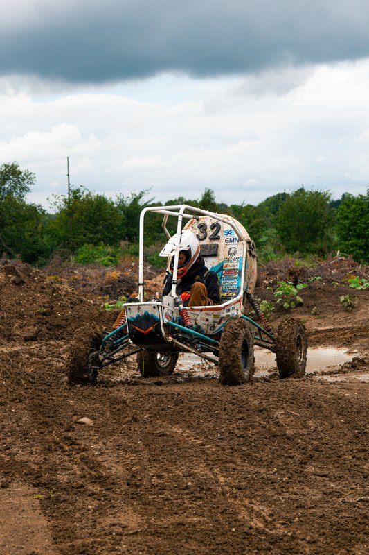 Baja car number 32 coming down a dirt mound toward the camera, vertical frame