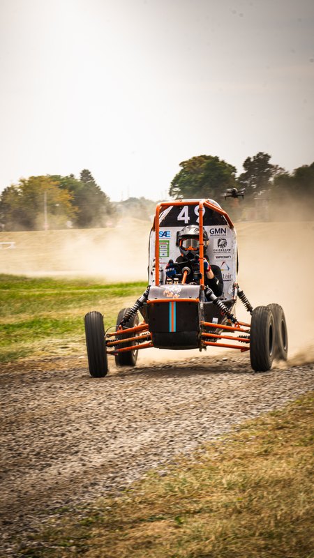 Vertical head-on shot of Baja car number 49 trailing dust along a gravel road
