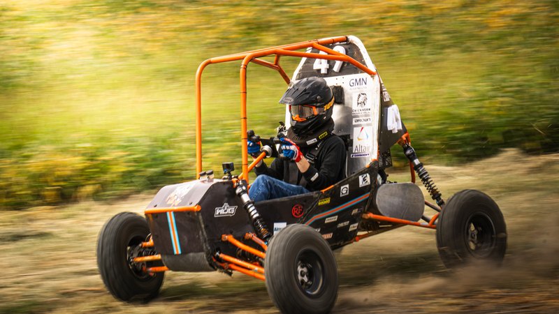 Orange Baja car number 49 in a tight panning shot, background streaked, dirt kicking off the rear