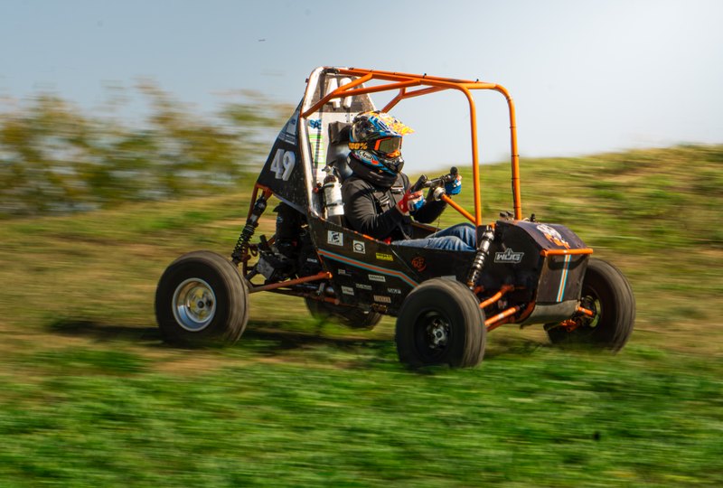 Baja car number 49 climbing a slope in a panning shot with open sky above
