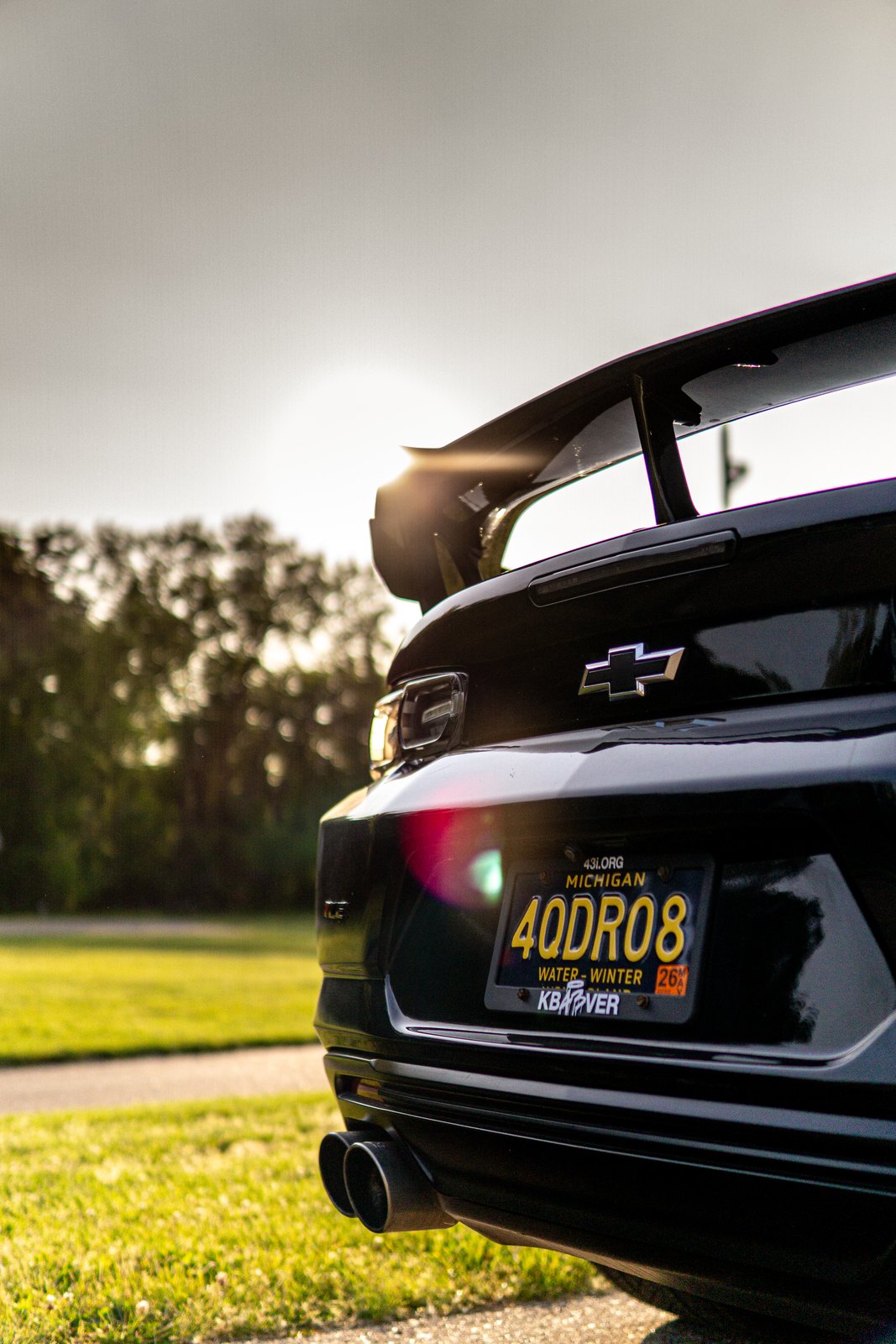 Backlit rear wing and rear end of a black Camaro with sun flare, vertical frame