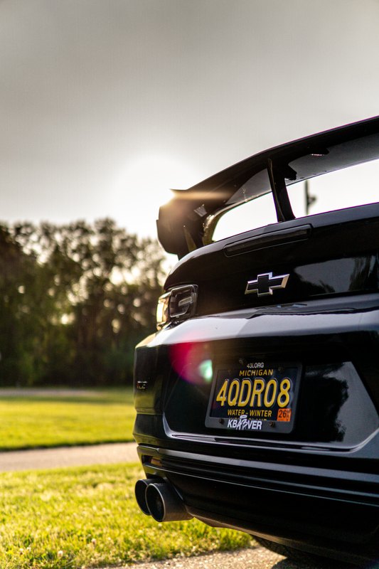 Backlit rear wing and rear end of a black Camaro with sun flare, vertical frame