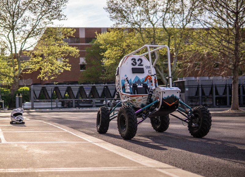 Baja car number 32, white bodywork with a teal frame, on pavement in a campus setting
