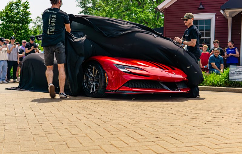 Red Ferrari being unveiled from a black cover in front of a crowd