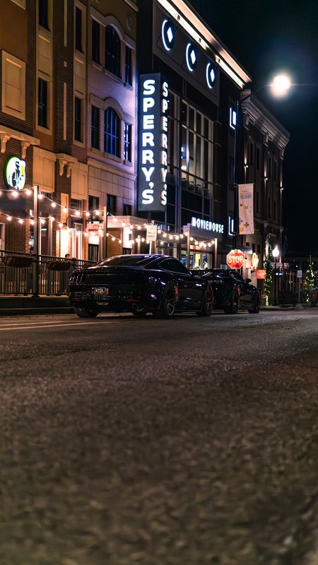 Vertical night street scene with neon theater signage and the two cars parked below