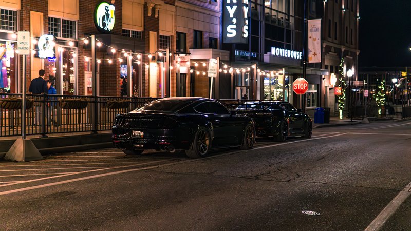 Black Mustang and Camaro on a lit downtown street at night