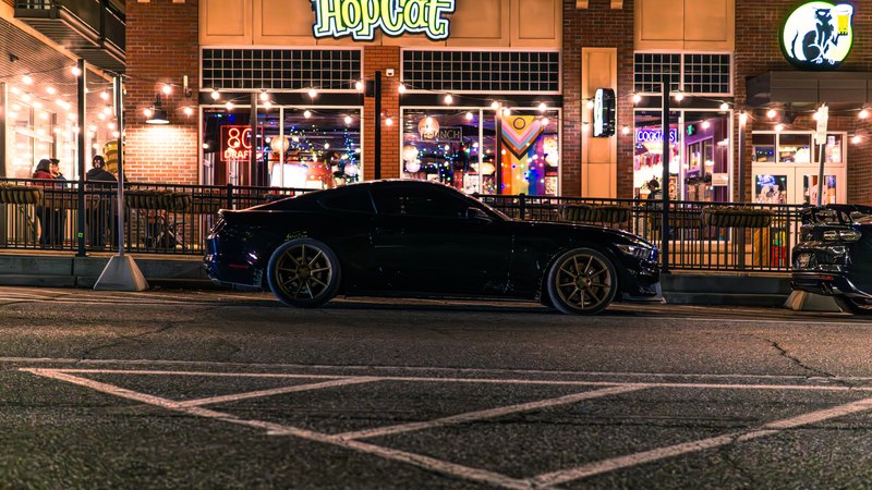 Black Mustang and Camaro on a lit downtown street at night